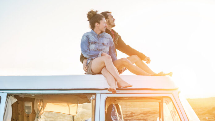 Happy,Couple,Sitting,On,Top,Of,Minivan,Roof,At,Sunset
