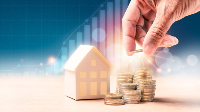 Businessman's,Hand,Putting,Coins,In,Stack,Near,Home,Model,With